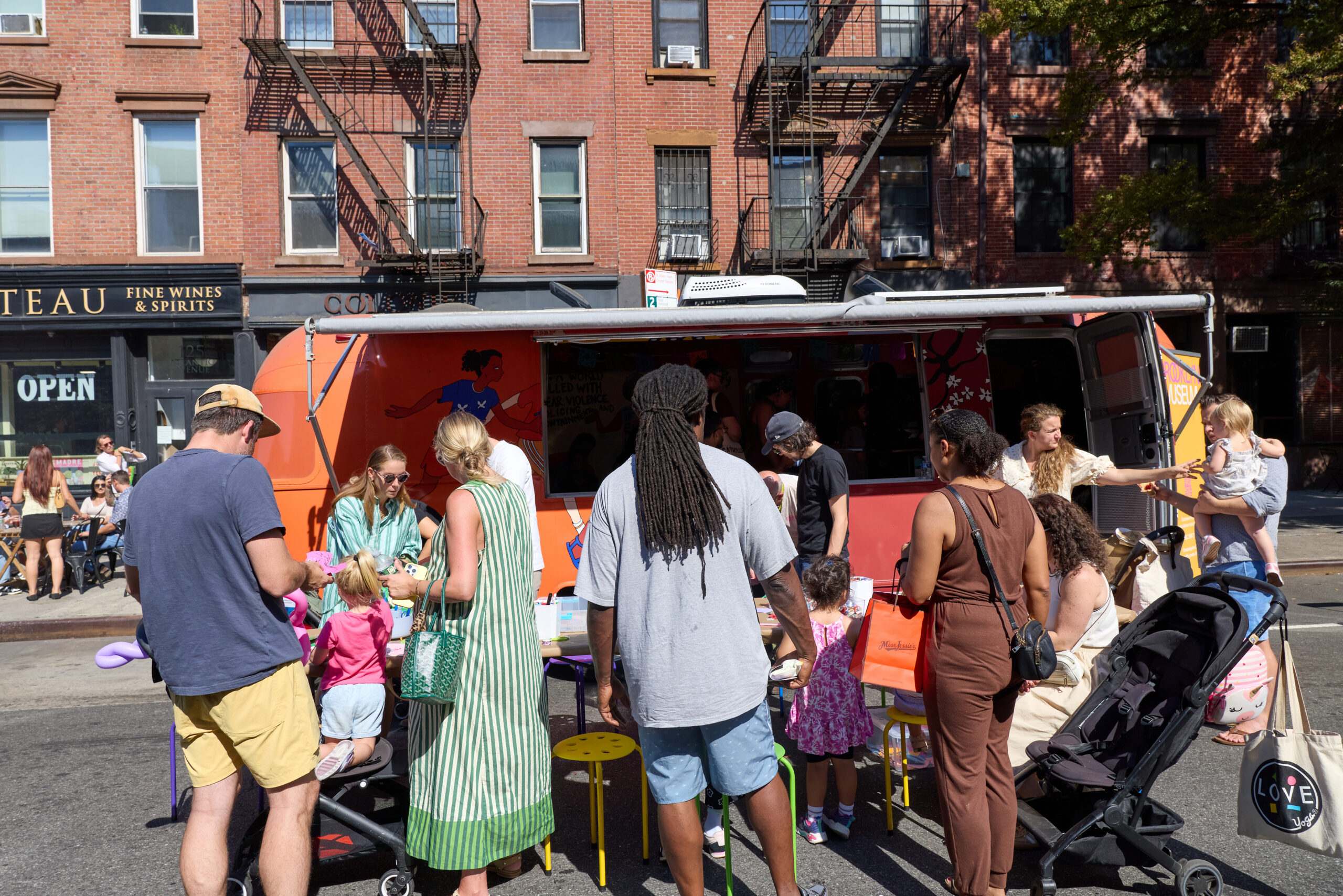 Families making art at the Brooklyn Museum orange Museum on Wheels truck parked on Atlantic Avenue