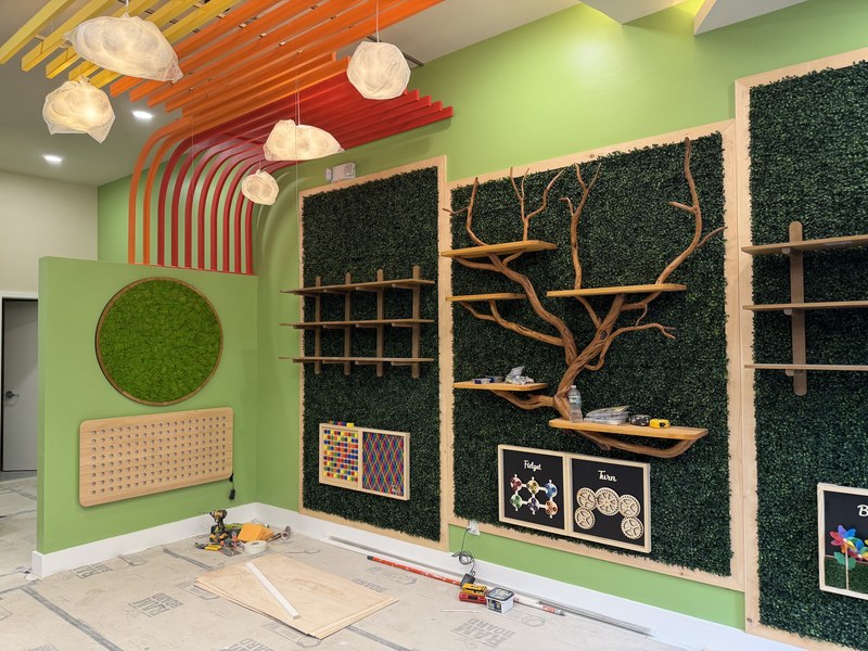 Inside Brooklyn Science Spot on Court Street before opening: green moss walls with wooden shelves on a branching tree, and orange ceiling arches