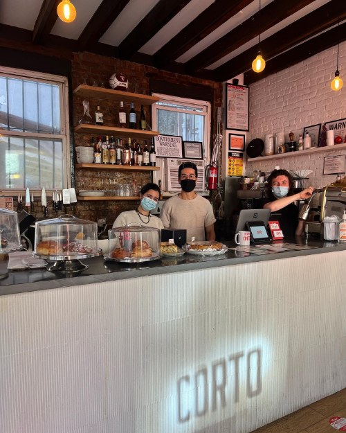 Inside Corto in Bed-Stuy: exposed brick, wooden beams and a counter with pastries under glass domes