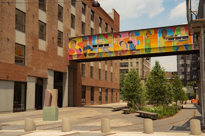 The brick courtyard at MADE Bush Terminal in Sunset Park, with a mural-painted skybridge between two buildings