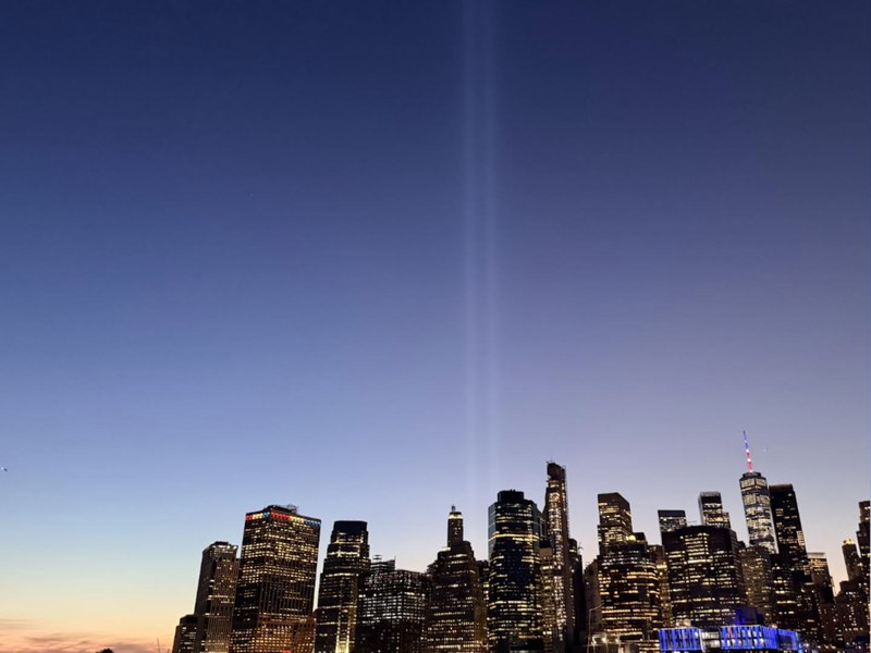 The Tribute in Light twin beams over the lower Manhattan skyline at dusk, seen from the Brooklyn waterfront