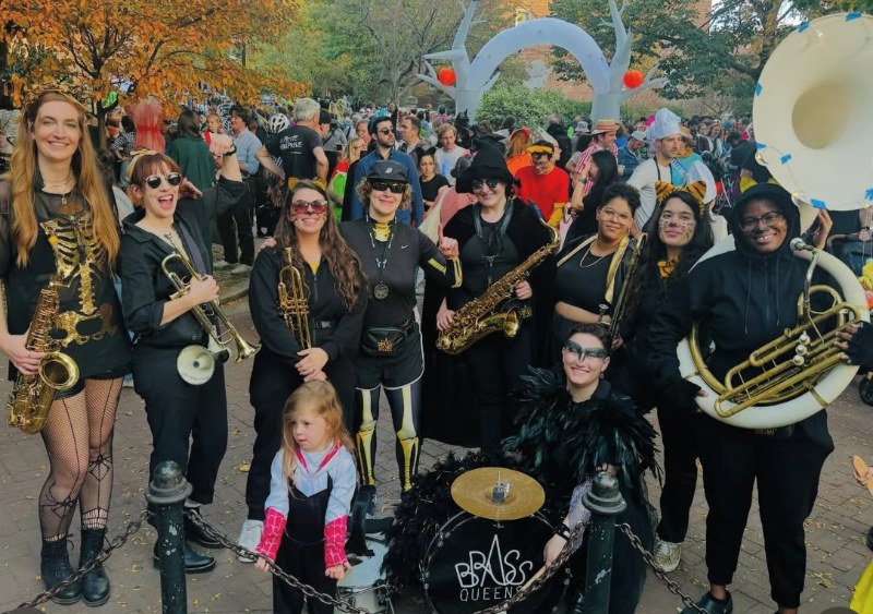 A brass band in Halloween costumes with a young trick-or-treater in Cobble Hill