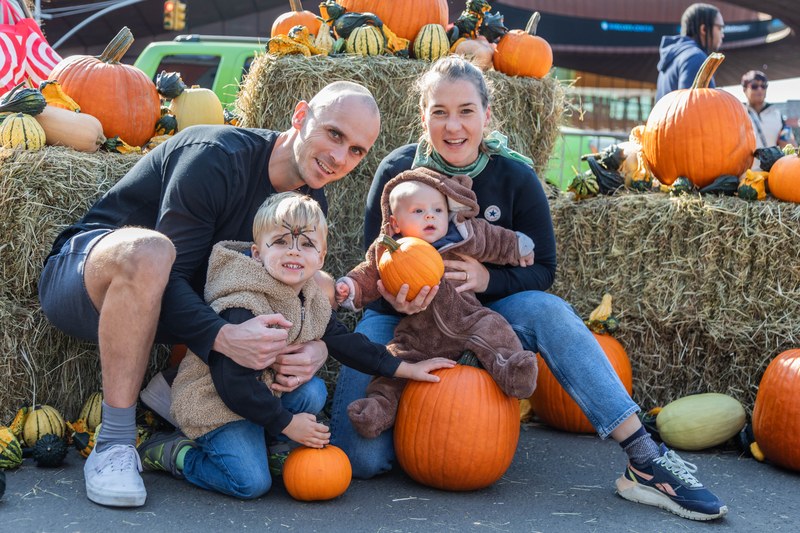 A family with two young children in costume posing with pumpkins and hay bales at Fall Fest at Atlantic Terminal Mall Plaza